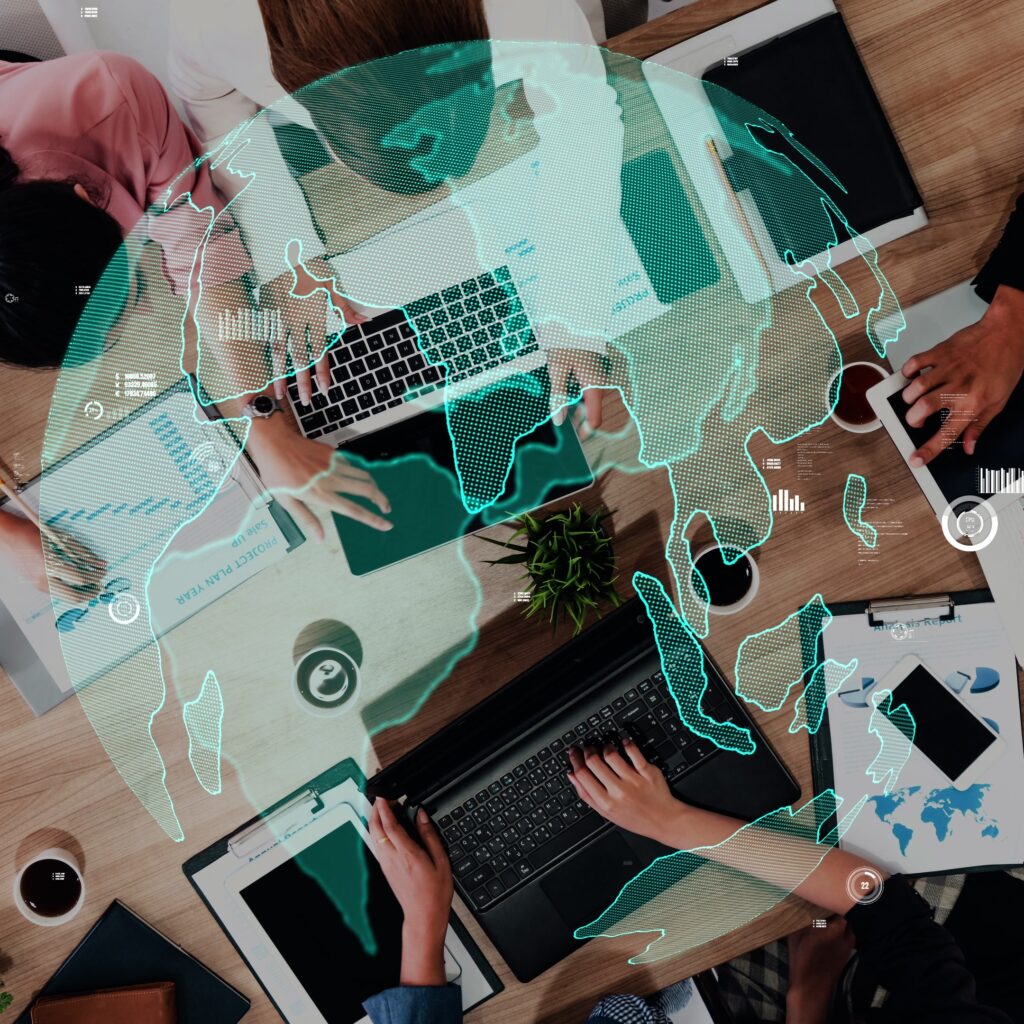 Team collaborating at a desk with a world map above, symbolizing global tech outsourcing opportunities.